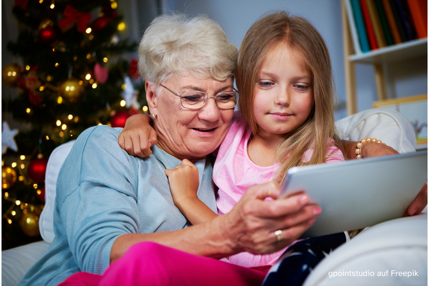 Ältere Damen schaut mit Enkelkind ins Tablet vor einem Christbaum